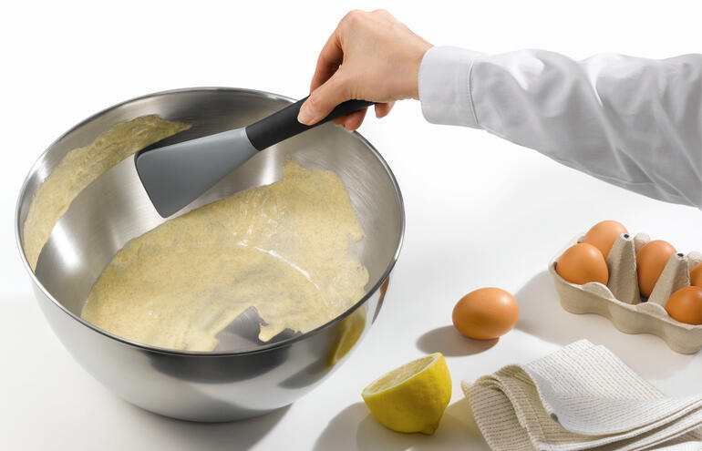Flexibele siliconen spatel die deeg uit een grote kom schept.