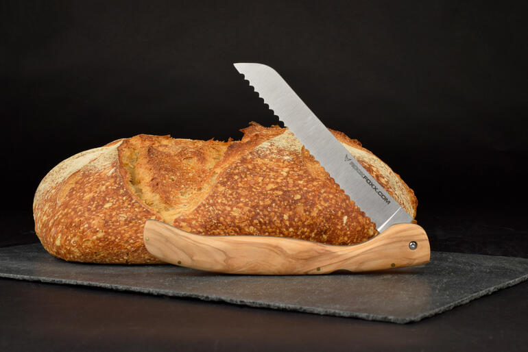 Opvouwbaar broodmes met olijfhouten handvat naast een brood op een zwarte ondergrond.