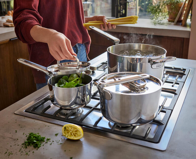 Kookgerei-set met opvouwbaar handvat, een pan en twee potten met groenten op het fornuis.