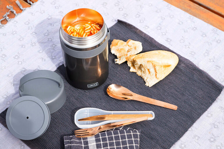 Geopende zwarte snackbox met verse pasta en brood op een tafel.