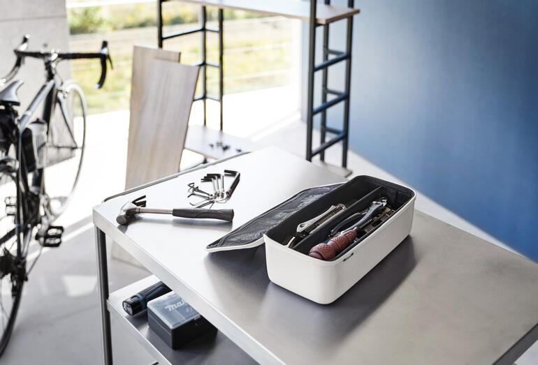 Gereedschapsdoos op een tafel met gereedschap op de achtergrond.