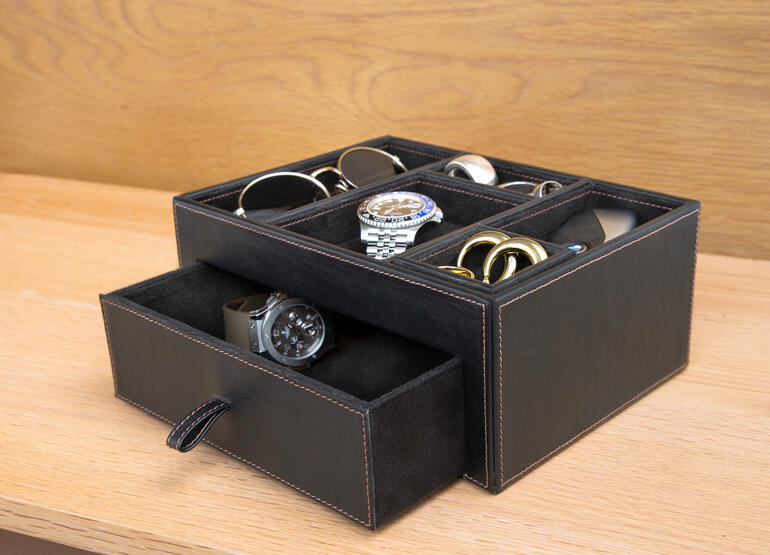 Zwarte leren opbergbox met verschillende accessoires zoals horloges en brillen.