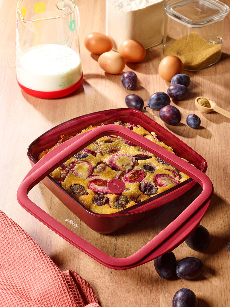 Rode ovenschaal met deksel, gevuld met een fruitschotel op een tafel.