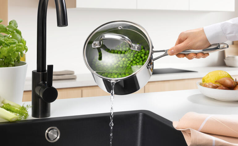 Steelpan met deksel, water wordt in de gootsteen gegoten.