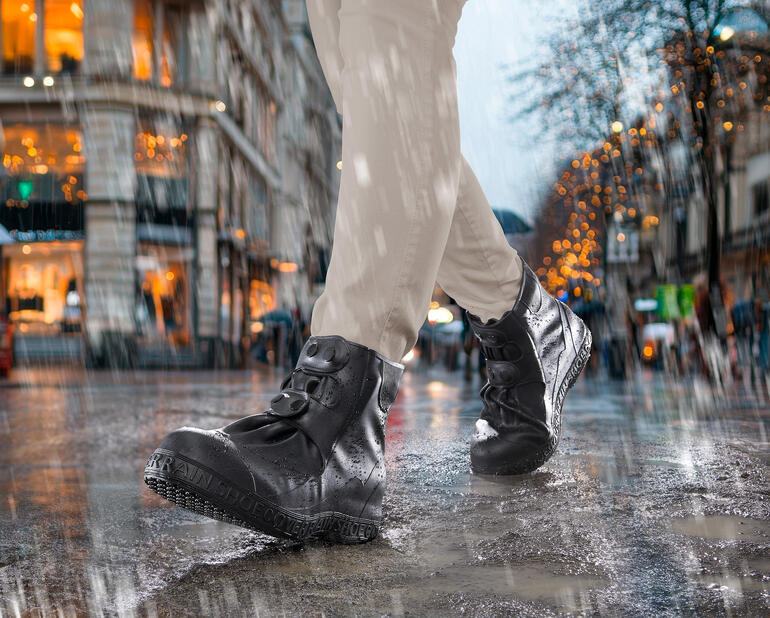 Persoon draagt zwarte laarzen met siliconen schoenovergangsnel in de regen op een natte straat.