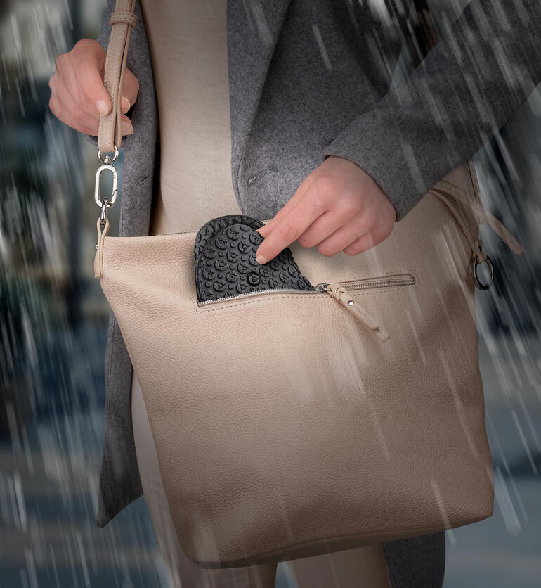 Persoon haalt een zwarte siliconen schoenovergangsnel uit haar tas in de regen.