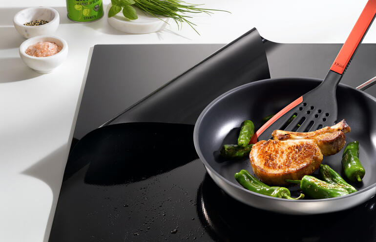 Koekenpan met courgette en een kotelet op een inductiekookplaatbescherming