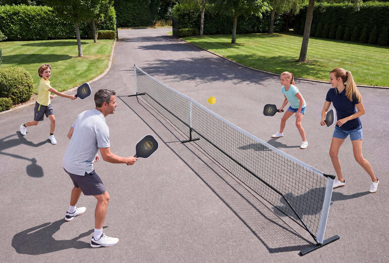 Gezin speelt Pickleball buiten, met net en ballen.