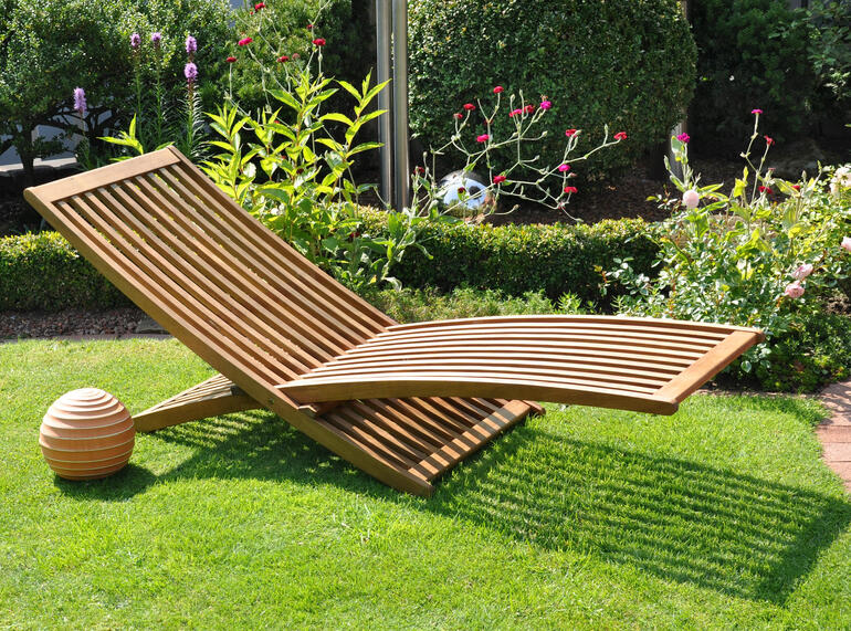 Houten ligstoel op groen gras in de tuin met bloeiende struiken.