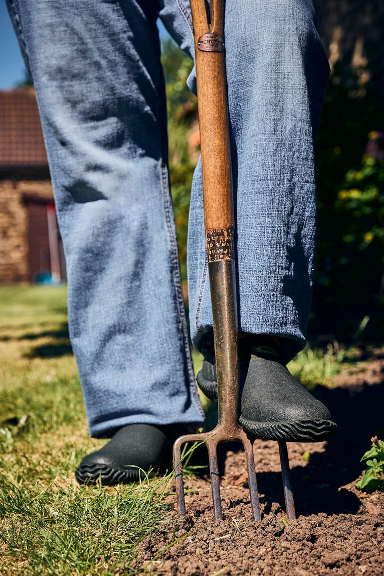 Persoon staat met tuinschep, draagt zwarte Airmesh tuinlaarzen.
