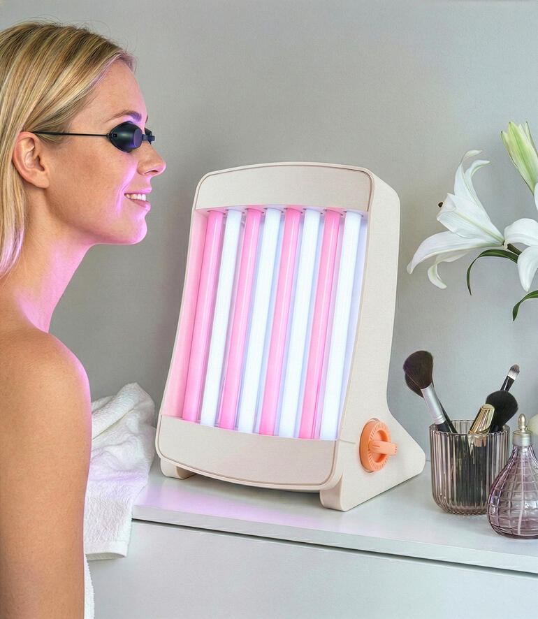 Gezichtsbruiner met roze en blauwe lampen, staat op een tafel naast cosmetica.