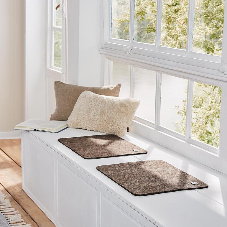 Twee lichtbruine alpaca-zitmatten op een vensterbank.