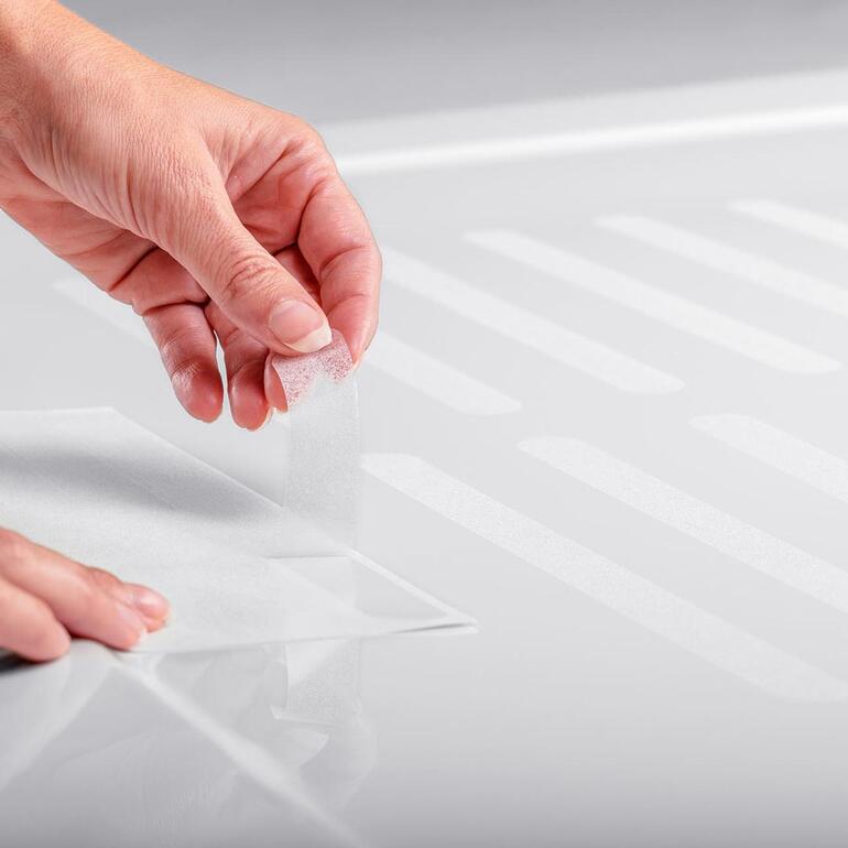Satho® antislipstrips, set van 10 Een hand plakt een antislipstrip op een douchevloer