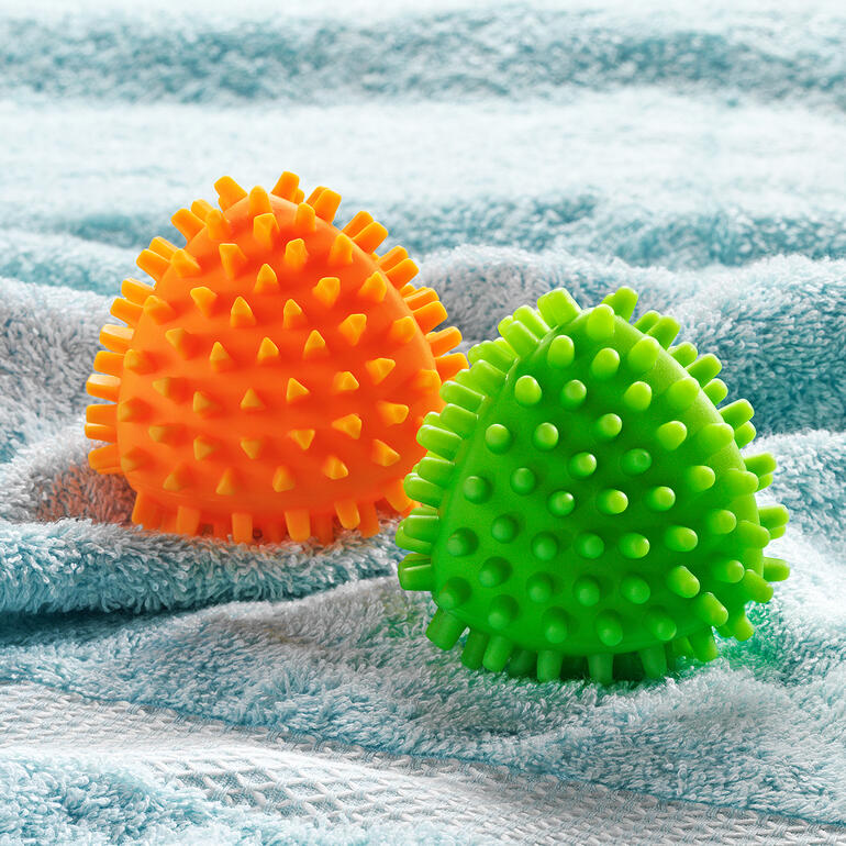 Twee droogballen in oranje en groen, op een handdoek.