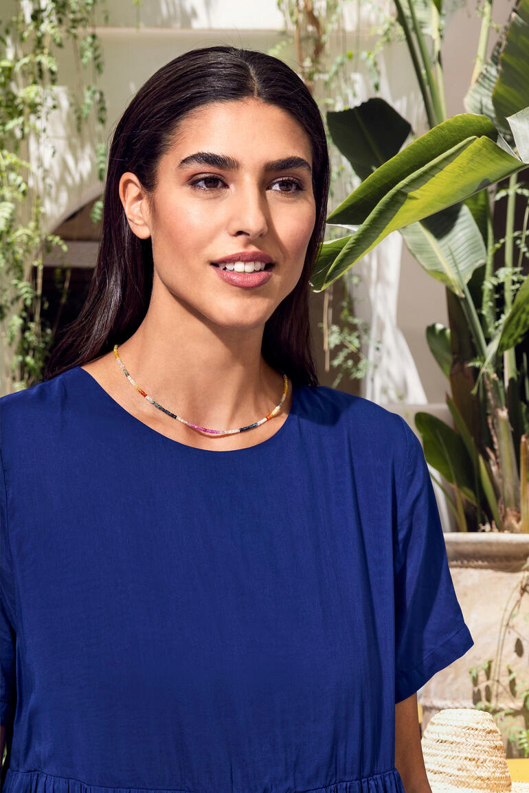 Saffierketting Vrouw met een saffierketting, glimlachend in de openlucht, omringd door planten.