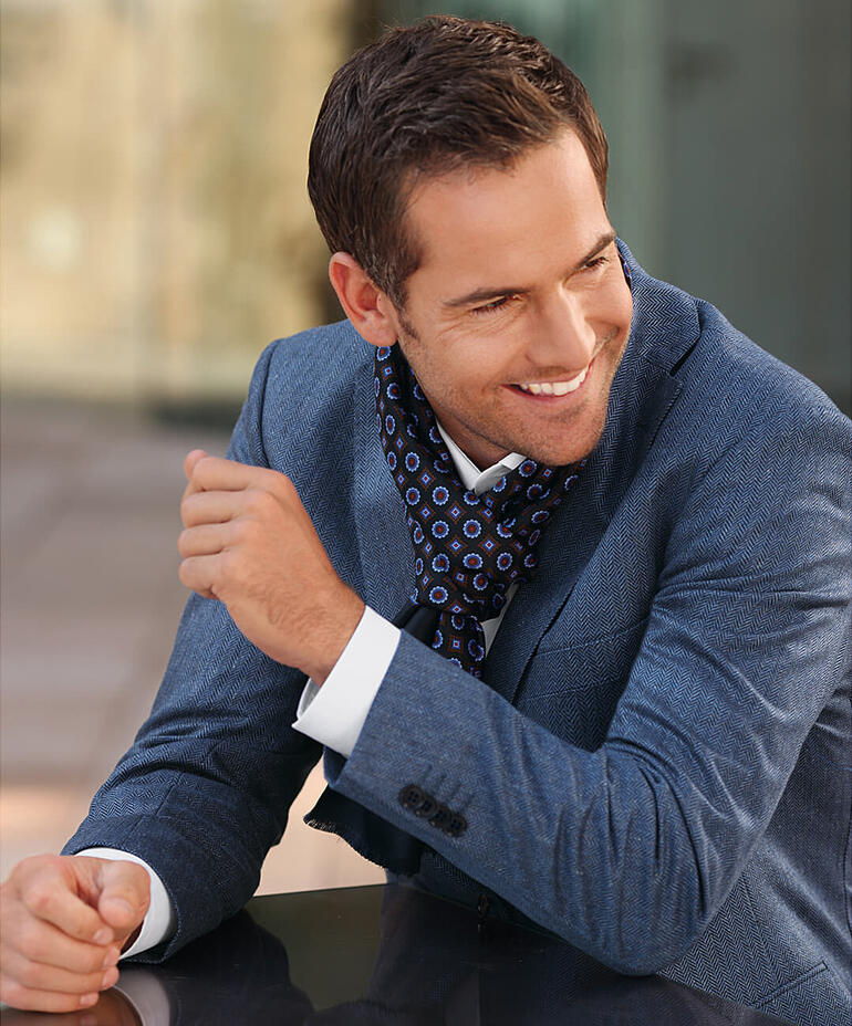 Glijdend man in een blauwe visgraat zijden blazer met een kleurrijke sjaal.