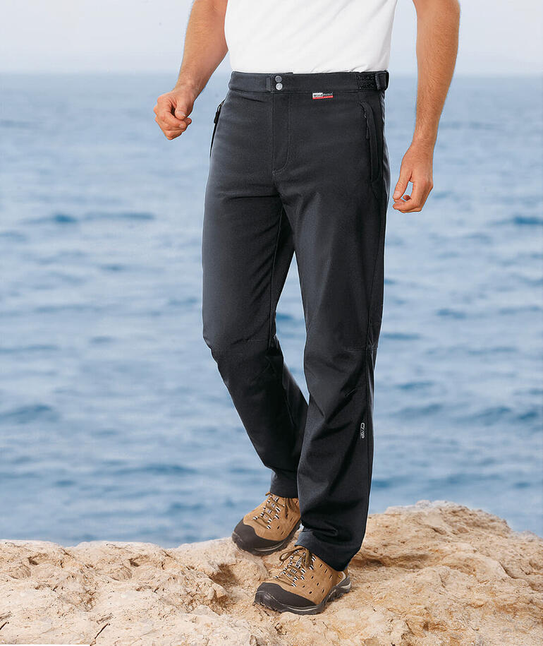 Man in zwarte softshell broek staat aan zee.