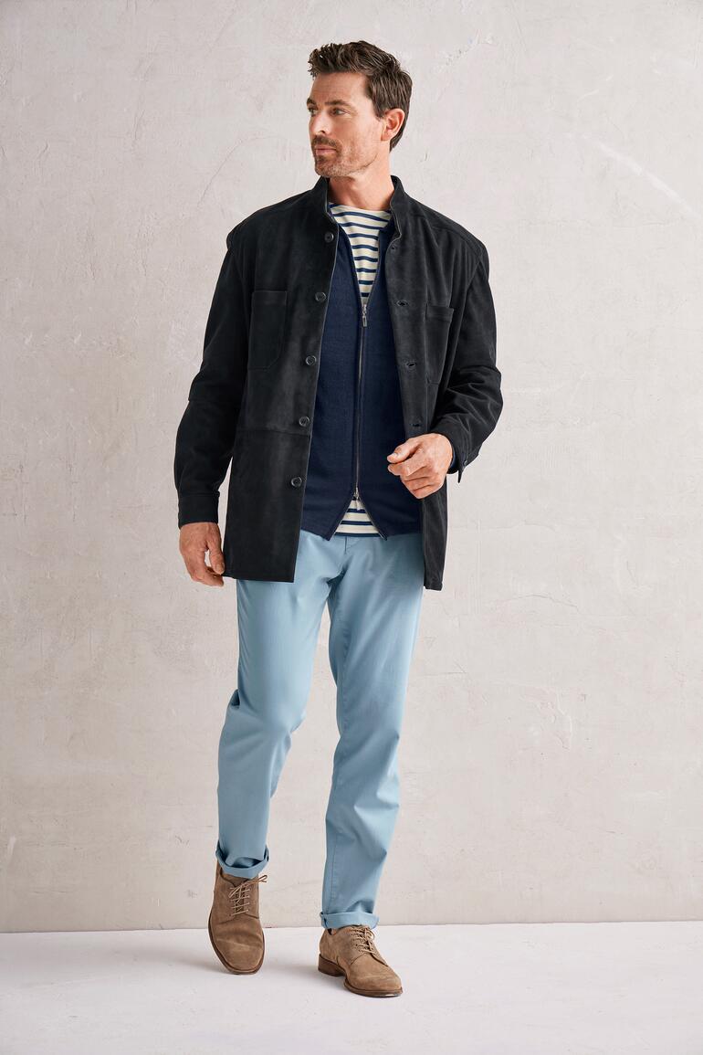 Man in een zwarte rendierkalfsleder hemdjack, staand in een lichte kamer voor een neutrale achtergrond.