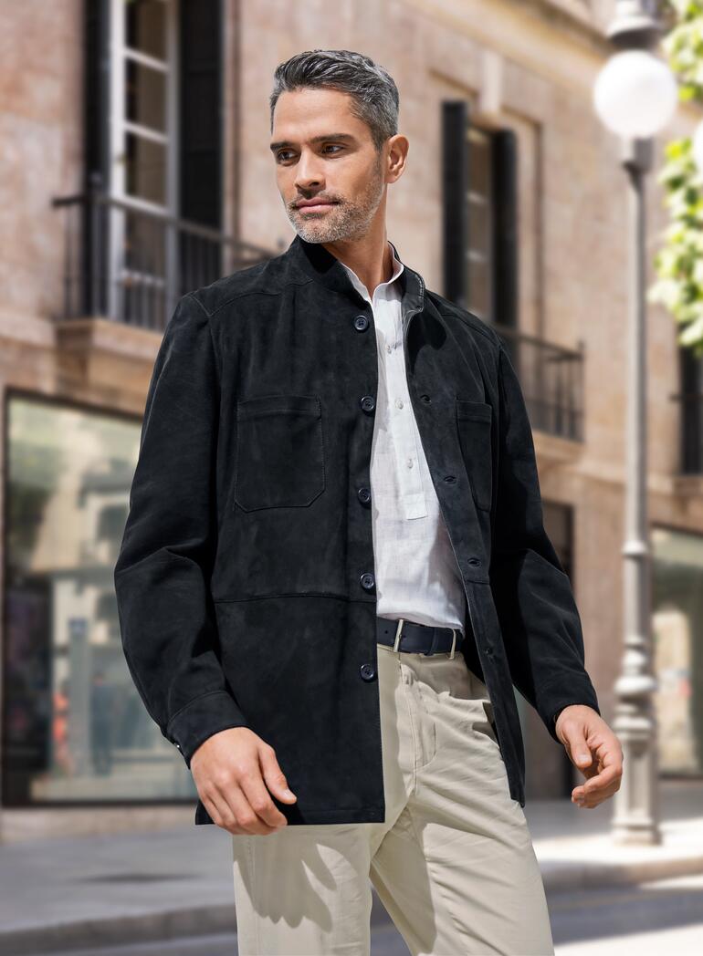 Man in een zwarte rendierkalfsleder hemdjack, staat in een stedelijke omgeving met een nadenkende uitdrukking.