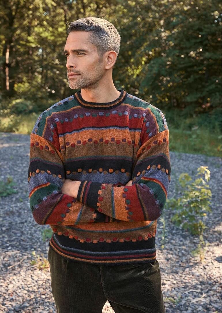 Man in kleurrijke trui staat in een groene omgeving.