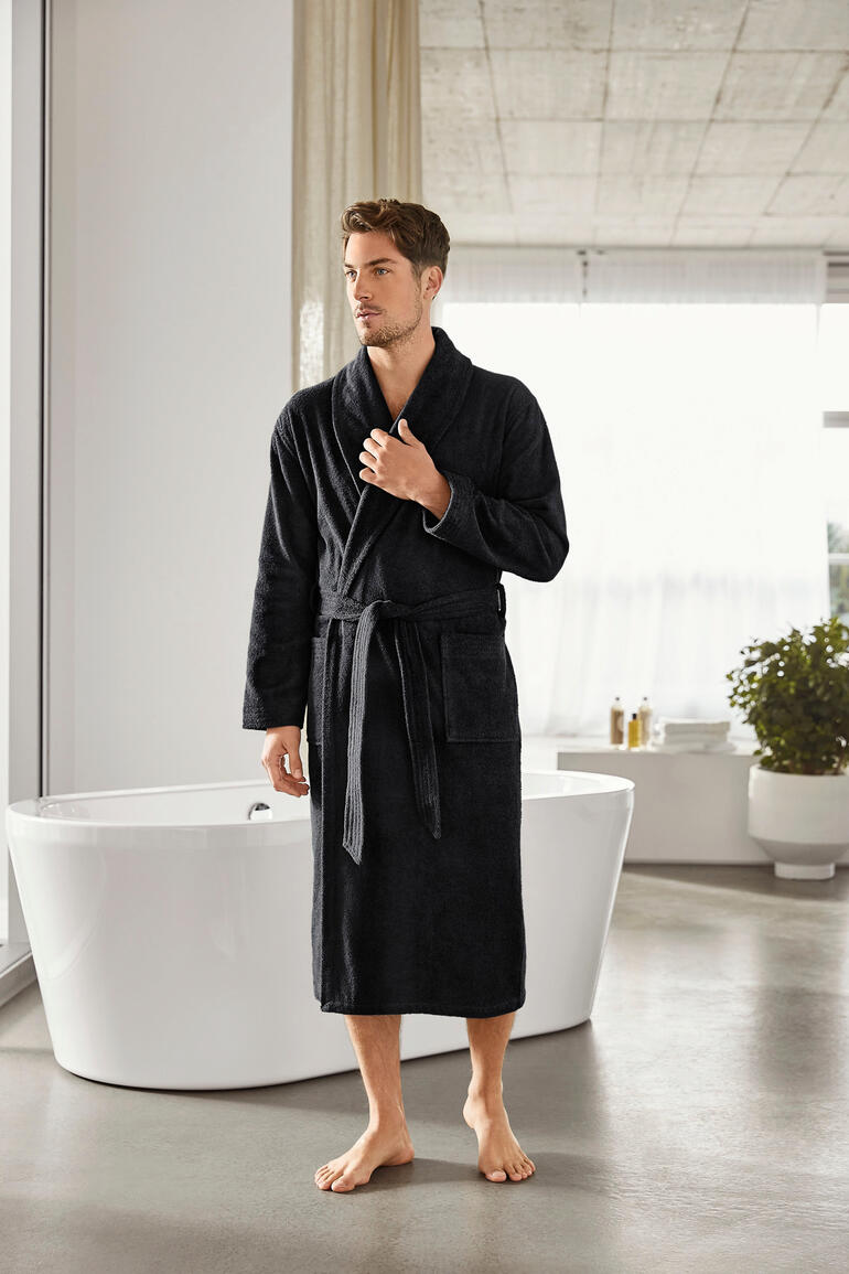Man in een zwarte badjas staat in een moderne badkamer