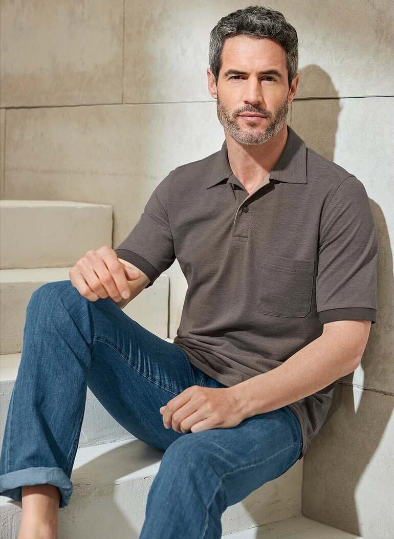 Man zit op een trap in een donker poloshirt en blauwe jeans.