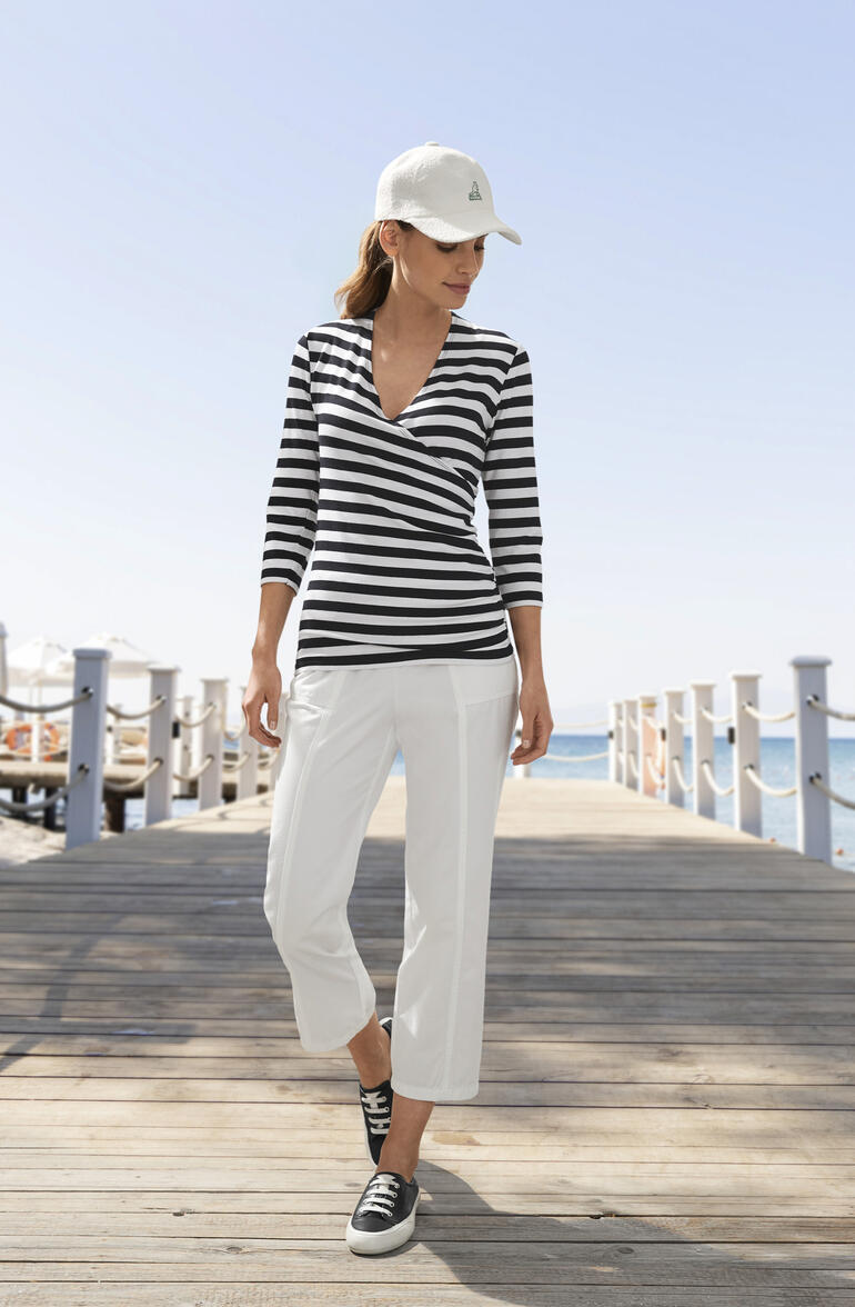 Vrouw in gestreepte blouse en witte broek, aan het strand.