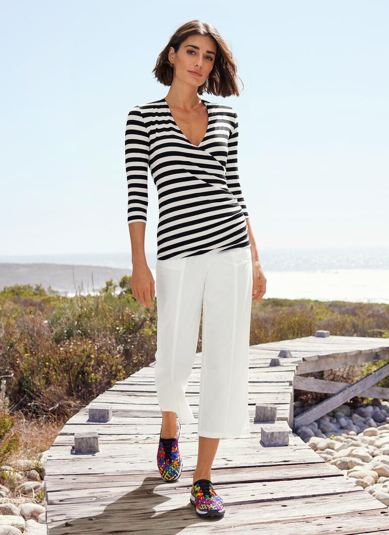 Vrouw in gestreepte blouse en witte broek, op houten steiger.