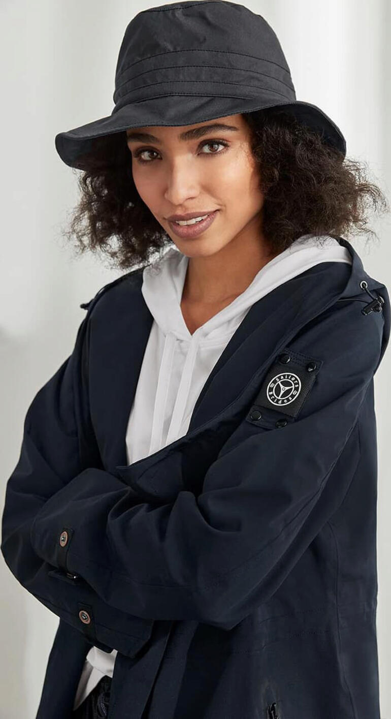 Vrouw met zwarte katoenen weerhoed en een donkergrijze jas glimlacht naar de camera.