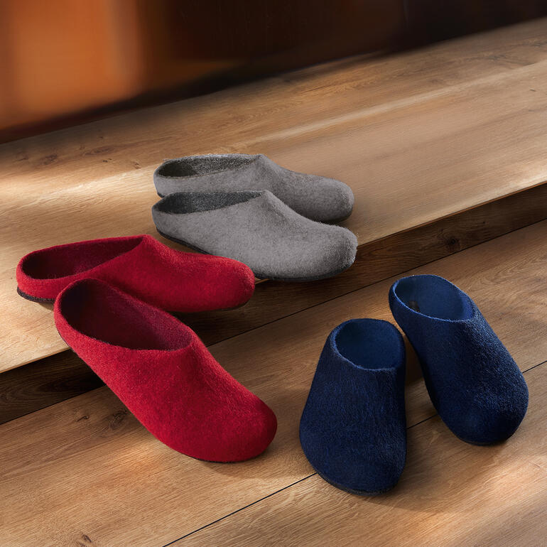 Vilten muil Diverse vilten slippers in rood, grijs en blauw op een houten vloer.