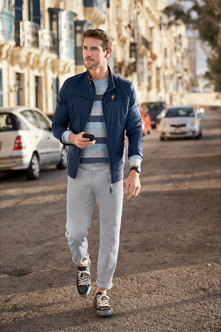 Steinbock® ultralicht-jack Man in een blauwe jas en grijze broek loopt naar een straat.