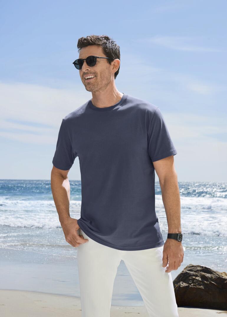 Man met een blauw T-shirt en een zonnebril op het strand.