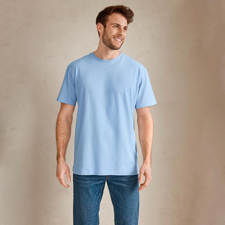 Man in een lichtblauwe T-shirt staat glimlachend voor een neutrale achtergrond.