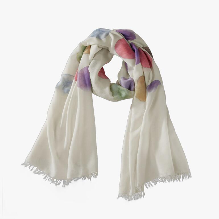 Kleurige aquarel stippen sjaal in crème, rood, paars en groen op een tafel.