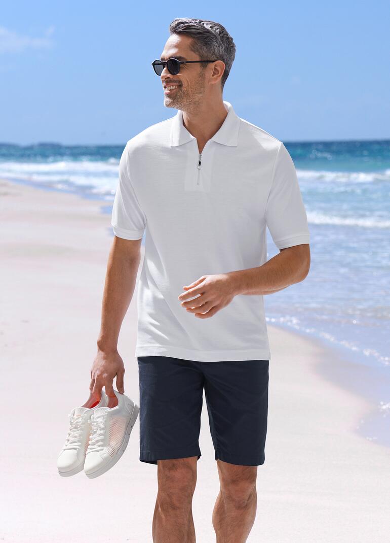 Man in wit poloshirt en zwarte shorts op het strand.