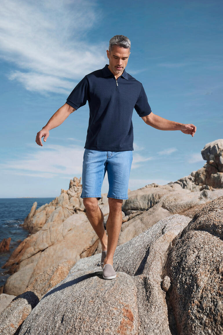 Man draagt navy Coolmax-korte mouw polo en staat op rotsen aan zee.