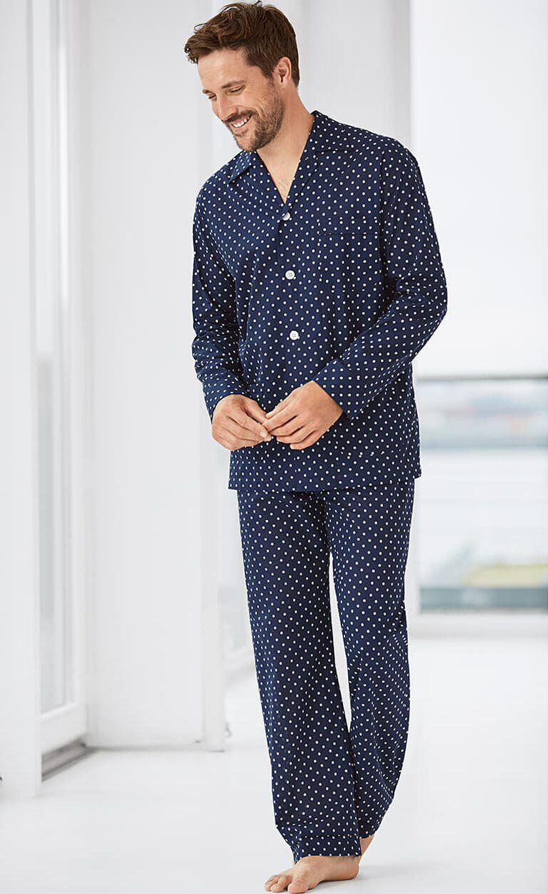 Man in een navy pyjama met witte stippen, glimlachend in de kamer.
