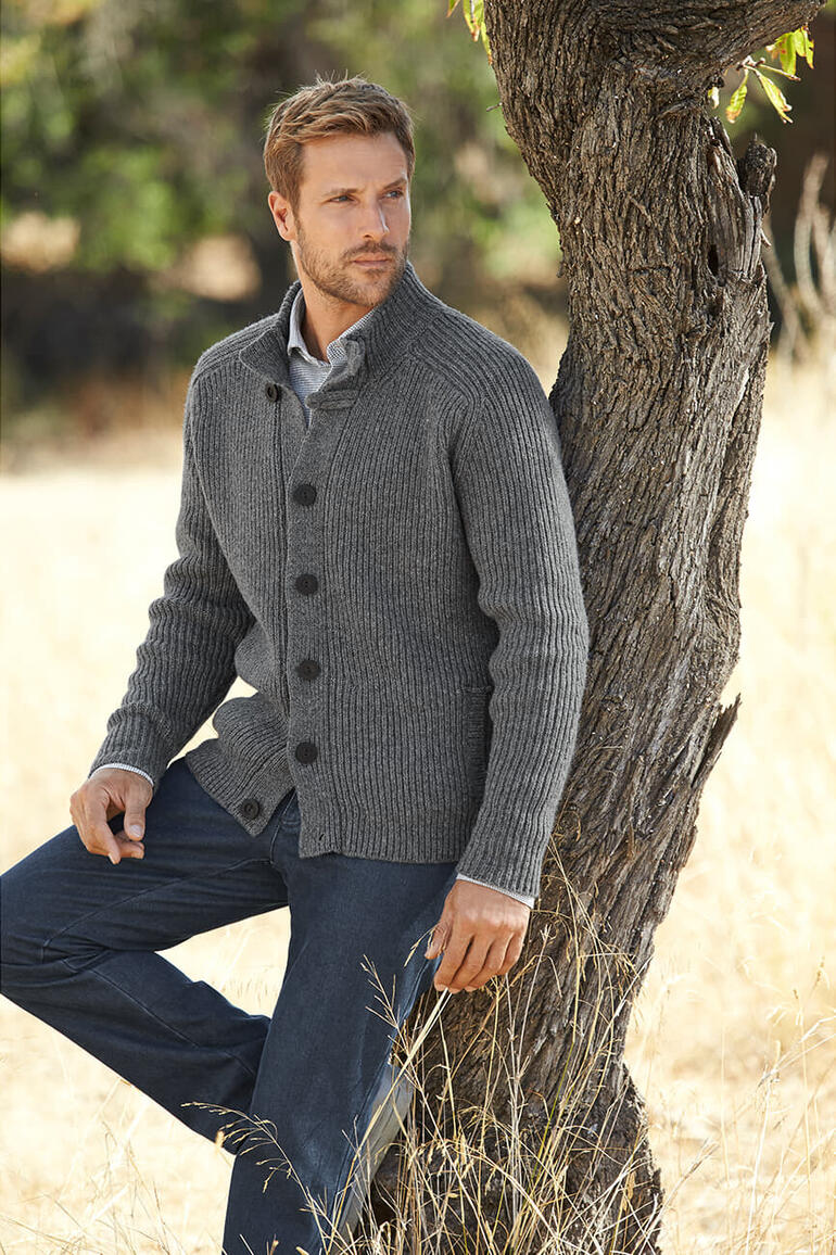 Man in grijze Fisherman Raglan Cardigan leunt tegen een boom.