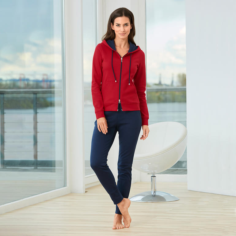 Vrouw in rode Pima-katoenen homesuit en blauwe broek staat in lichte kamer