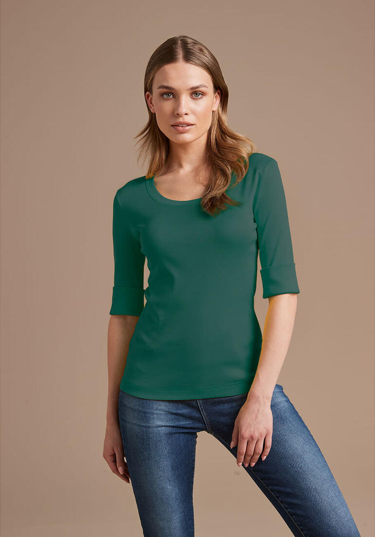 Vrouw in groen Wolff-shirt met 3/4 mouwen poseert voor een neutrale achtergrond