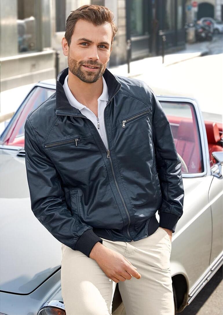 Man poseert in een blauwe leren zomerblouson voor een auto.