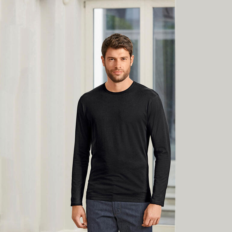 Man in zwart Sunspel-shirt, staat in een kamer met heldere ramen.