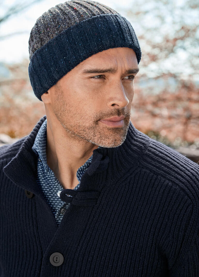 Man draagt een gestreepte Donegal muts van wol, met een neutrale gezichtsuitdrukking.