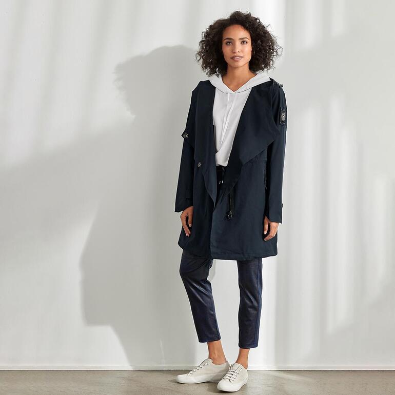 Vrouw in softshell jas met capuchon, staande in een lichtgekleurde ruimte.