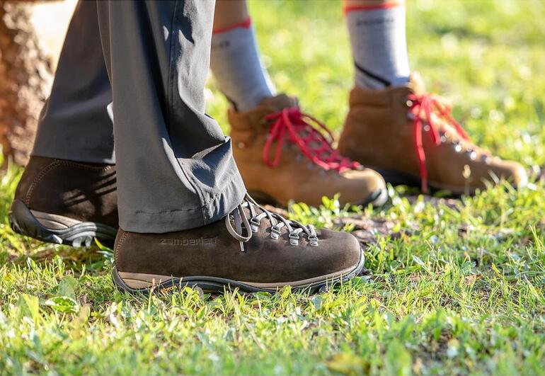 heren, donkerbruin en dames, bruin Zamberlan® wandelschoenen, voeten van een persoon in een bruine en een beige schoen op het gras.