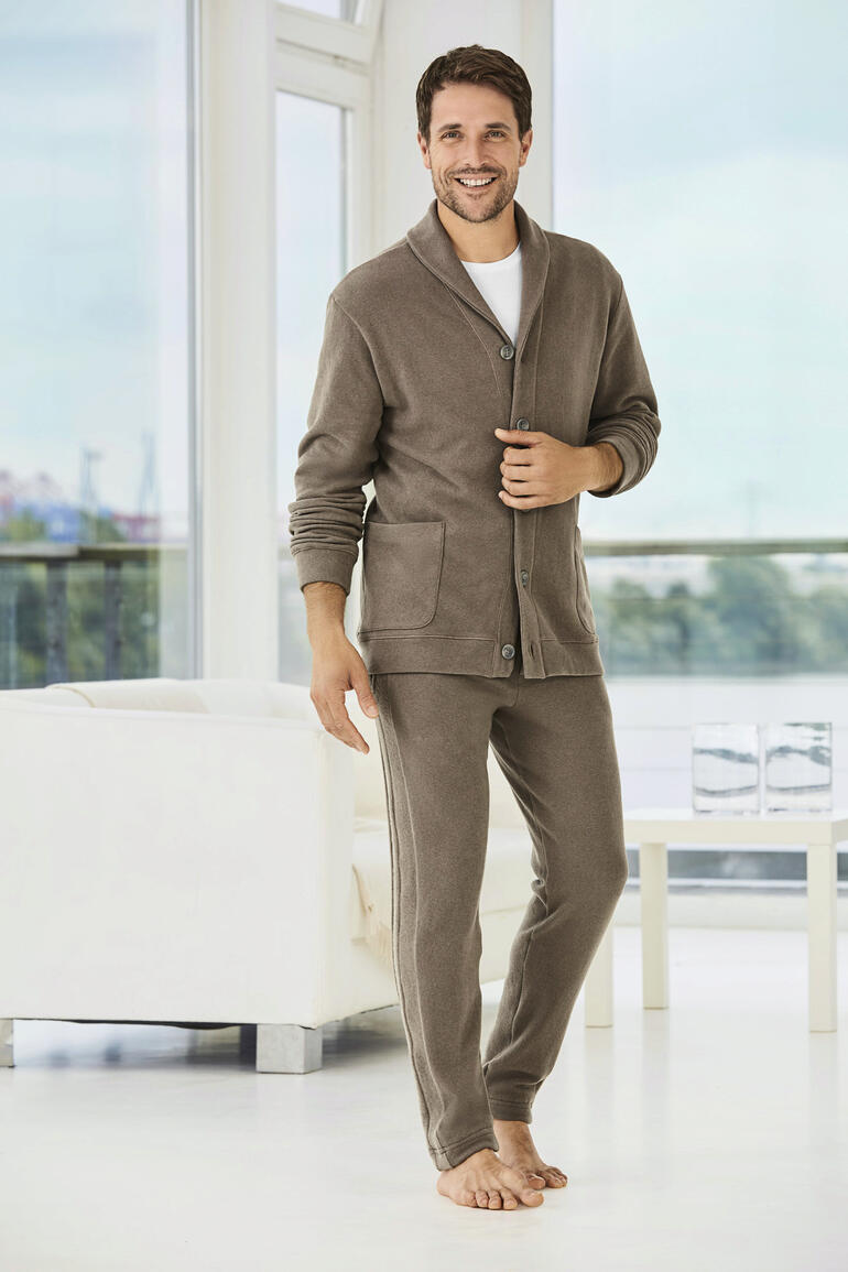Zimmerli Gentleman Homesuit - Het huispak voor de gentleman: Italiaanse Jersey. Elegante snit. Modieuze details. Van Zimmerli. Man in een beige huispak met zakken, staat in een lichte kamer.