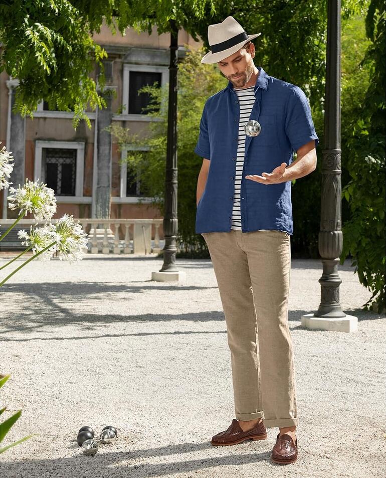 bruin Man in een blauwe Dorani vintage linnenhemd, staat in een tuinlandschap.