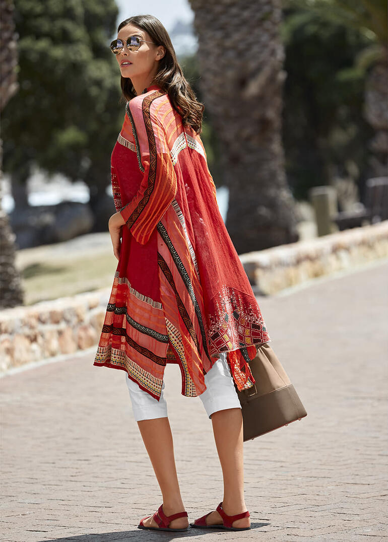 Vrouw in rood met IVKO kimono-vest, staat met een handtas op een pad