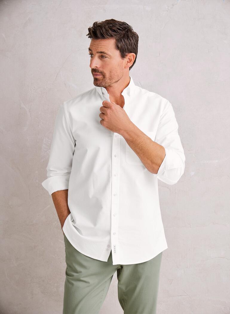 Man in wit overhemd met groene achtergrond staat nadenkend.