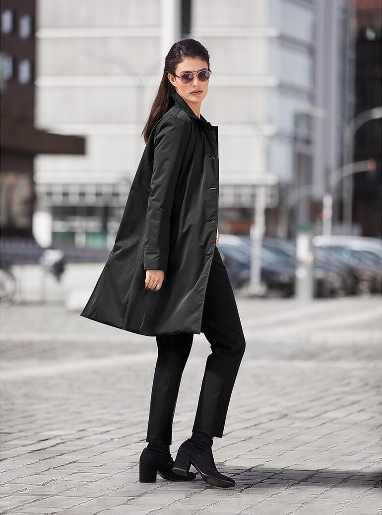 Vrouw in zwarte reismantel in een stedelijke omgeving